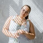 plus size woman in tank top holding flowers with sunlight filtering through blinds. 8433431 scaled