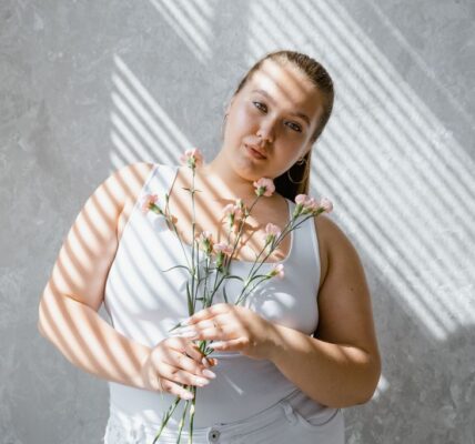 plus size woman in tank top holding flowers with sunlight filtering through blinds. 8433431 scaled