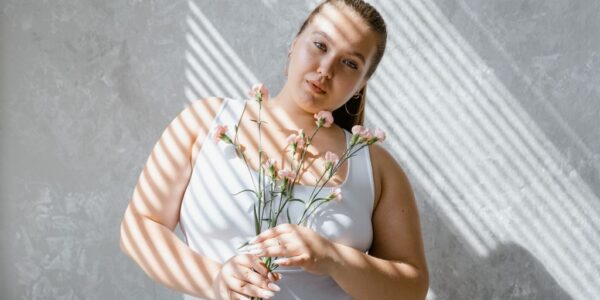 plus size woman in tank top holding flowers with sunlight filtering through blinds. 8433431 scaled