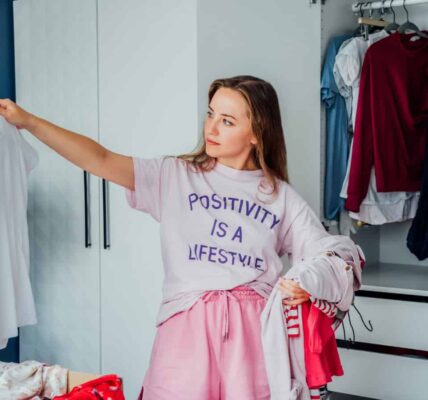 Woman selecting clothes from her wardrobe for donating to a Charity shop. Decluttering Sorting clothes and Cleaning Up. Reuse second hand concept. Conscious consumer sustainable lifestyle