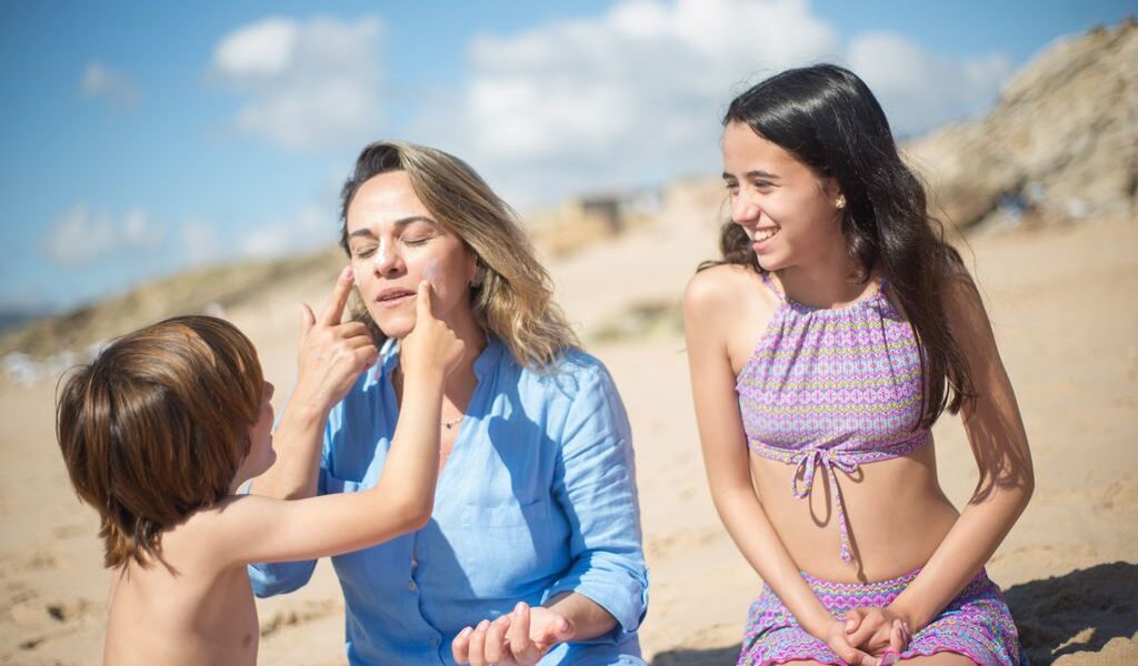 A mother with her kids applying sunscreen on a sunny beach in Portugal.